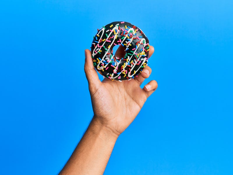 Hand of hispanic man holding chocolate donut over isolated blue background.