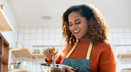 Young African American woman enjoying herself cooking in kitchen while staying at home