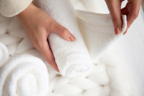 Woman in beige warm robe is folding the clean white hand towels and putting into a metal mesh basket...