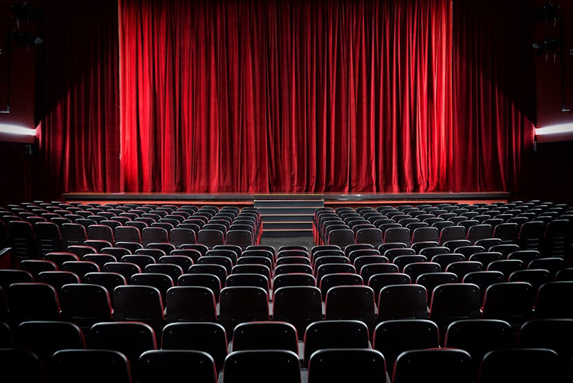 Darkened empty movie theatre and stage with the red curtains drawn viewed over rows of vacant seats ...