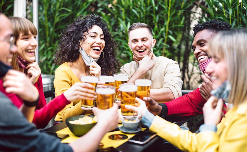 Young people toasting beer wearing open face mask - New normal life style concept with friends havin...