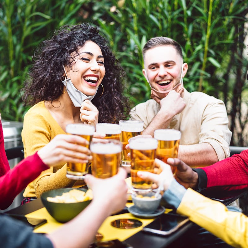 Young people toasting beer wearing open face mask - New normal life style concept with friends havin...