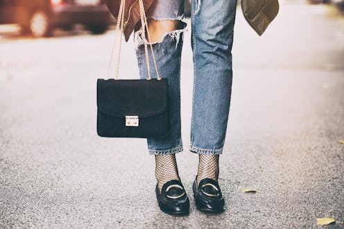 fall fashion outfit details. fashionable woman wearing ripped jeans with loafers, fishnet stockings,...