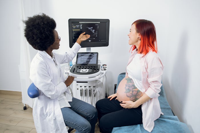 Beautiful young red haired pregnant woman in modern clinic, looking at the screen of ultrasound mach...
