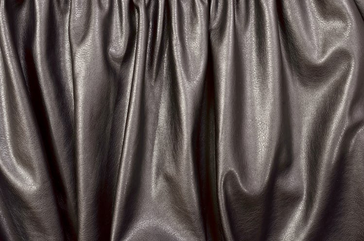 Close up on crumpled black leather material textured fabric. Shiny black pleather as a background.