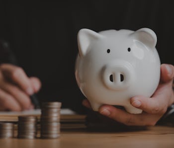 Man hand holding piggy bank on wood table, saving money wealth and financial concept, Business, fina...