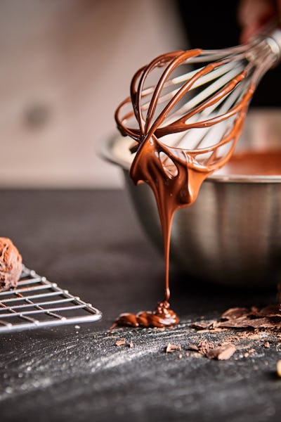 Baker or chocolatier preparing chocolate bonbons whisking the melted chocolate with a whisk dripping...