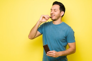 Attractive latin man eating a big chocolate candy bar. Handsome man in his 30s with sugar cravings e...