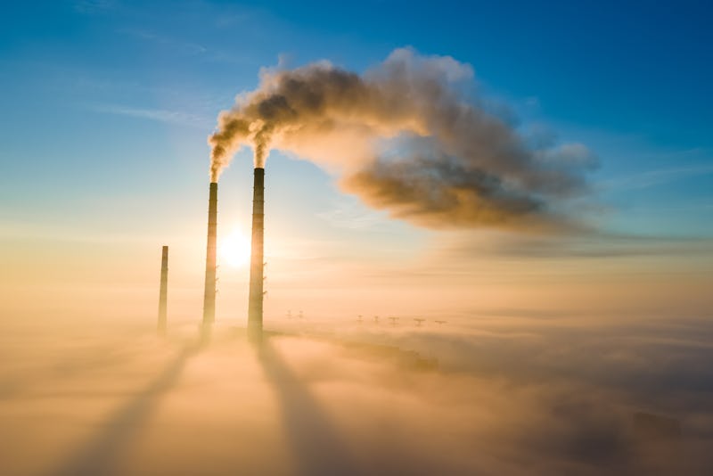 Aerial view of coal power plant high pipes with black smoke moving up polluting atmosphere at sunset...