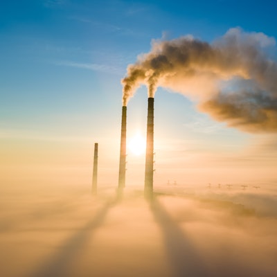 Aerial view of coal power plant high pipes with black smoke moving up polluting atmosphere at sunset...