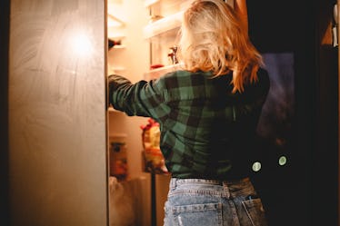 Young hungry woman looking for food in fridge at night at home