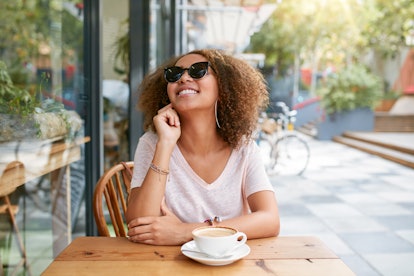 A happy young woman sits outside at a cafe. A key to success is to think bigger than you are and sta...