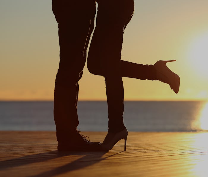 Couple legs silhouette hugging in love on the beach with the sun in the background at sunset