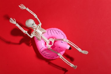 Toy skeleton with inflatable flamingo on red bright background. Halloween theme. Beach vacation conc...