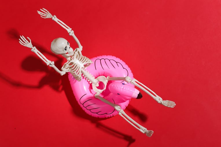Toy skeleton with inflatable flamingo on red bright background. Halloween theme. Beach vacation conc...