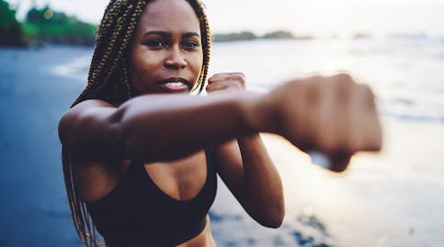 African American fit girl in tracksuit practice power punches on seashore, concentrated sportswoman ...