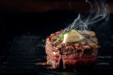 A steaming beef tenderloin steak is grilled in a grill pan with the text copy space. The concept of ...