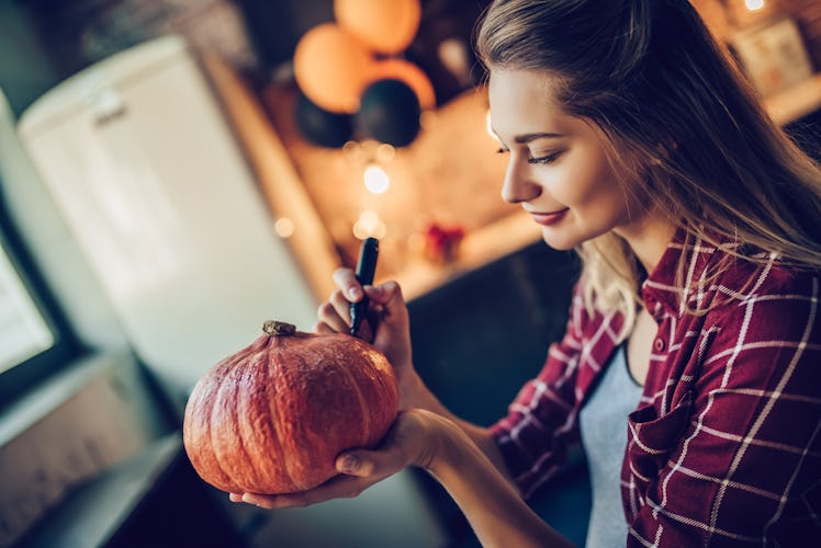 Young woman drawing on pumpkin around Halloween after learning her October 2021 monthly horoscope.