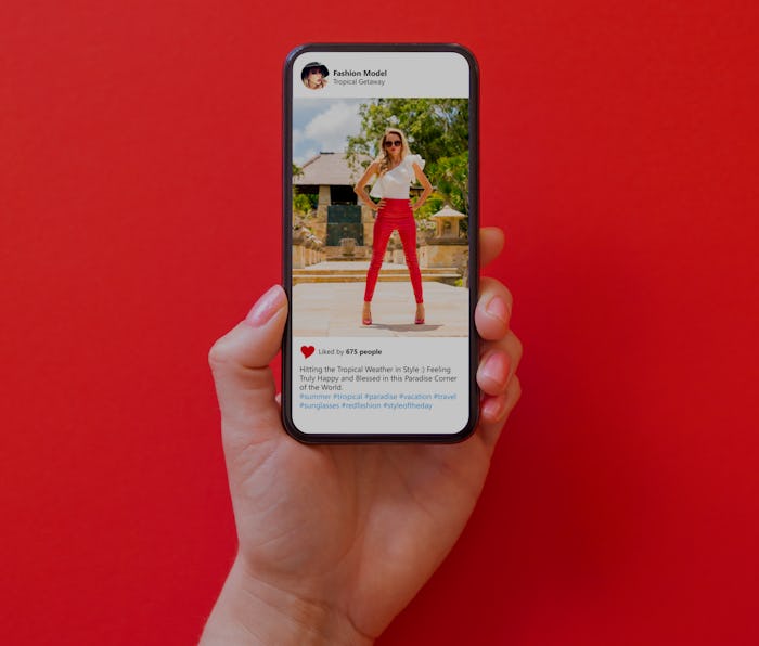 Woman holding phone in hand with photo of fashion model in red pants on red background