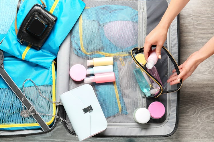 Female hands, bag with travel cosmetics kit and suitcase on floor