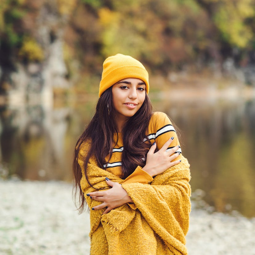 Young woman in yellow beanie standing in the forest during fall, affected by the October 2021 new mo...