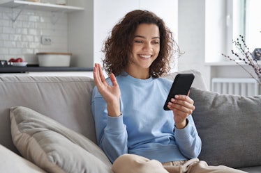 Happy hispanic teen girl waving hand using smartphone app enjoying online virtual chat video call wi...