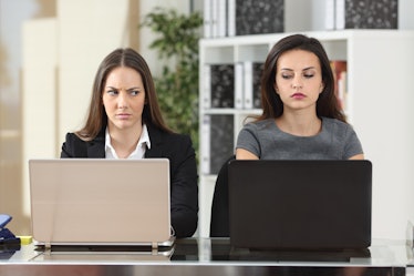 Front view of two angry businesswomen looking each other with hate working with laptops at office