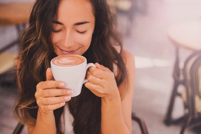 Young beautiful happy woman with long curly hair enjoying cappuccino, her go-to Starbucks order acco...