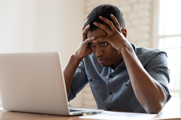 Mad African American young male employee look at laptop screen having operational software problems,...