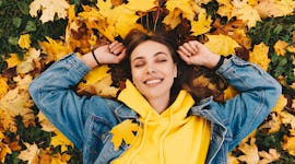 Young woman laying in leaves during fall, having the best week of October 18, 2021, per her zodiac s...