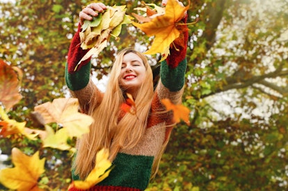 Joyful girl throws leaves in autumn park. Woman feel good outdoors in fall. Happy smiling person in ...