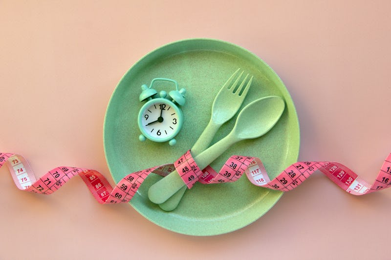 Creative flat lay composition with plate, alarm clock, spoon, fork and measuring tape on pink backgr...