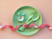 Creative flat lay composition with plate, alarm clock, spoon, fork and measuring tape on pink backgr...