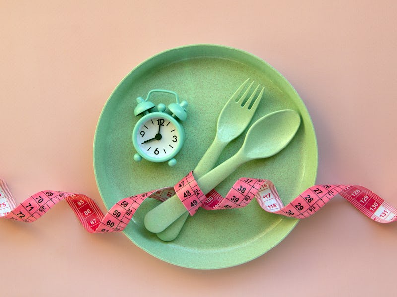 Creative flat lay composition with plate, alarm clock, spoon, fork and measuring tape on pink backgr...
