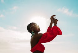 A woman wearing a bright red shirt is dancing outside in the sunshine. The April 2022 new moon in Ar...