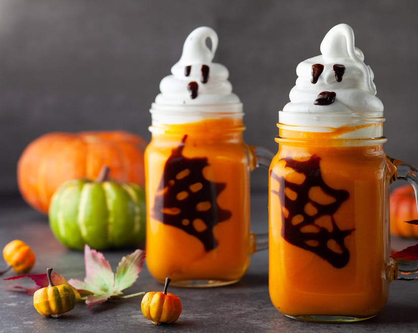Halloween Pumpkin cocktail with whipped cream in ghost shape and chocolate spider web. Freakshake f...