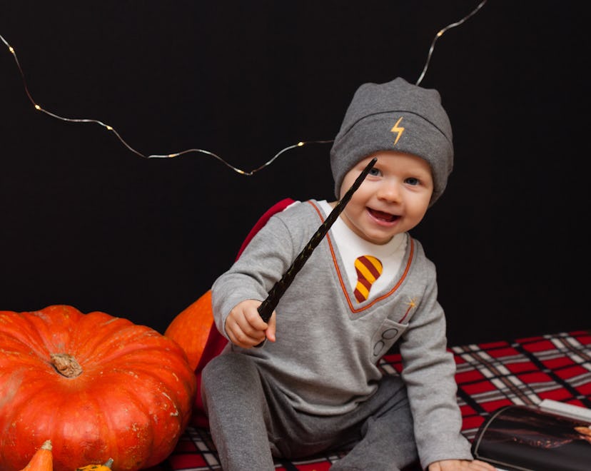 Little baby boy is reading a magic book in halloween time. Magic wand in a hand, black background an...