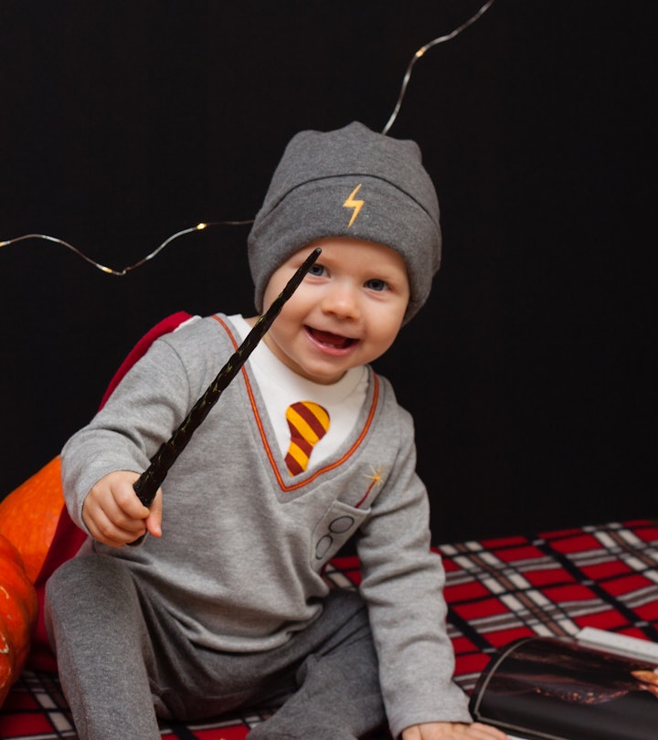 Little baby boy is reading a magic book in halloween time. Magic wand in a hand, black background an...