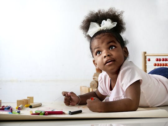 A Cute and adorable African girl lay down on the floor and drawing a picture with color pencil in th...