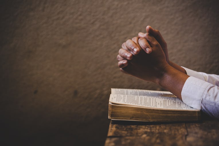 Hands folded in prayer on a Holy Bible in church concept for faith, spirituality and religion, woman...