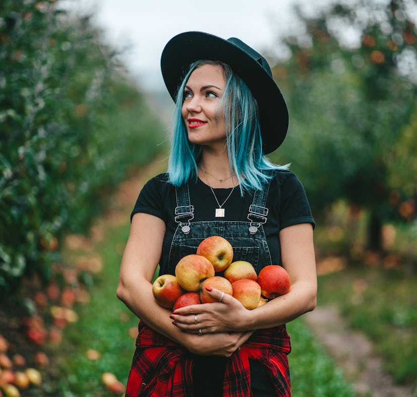 Blue haired woman picked up a lot of ripe red apple fruits in October 2021, the best month for her z...