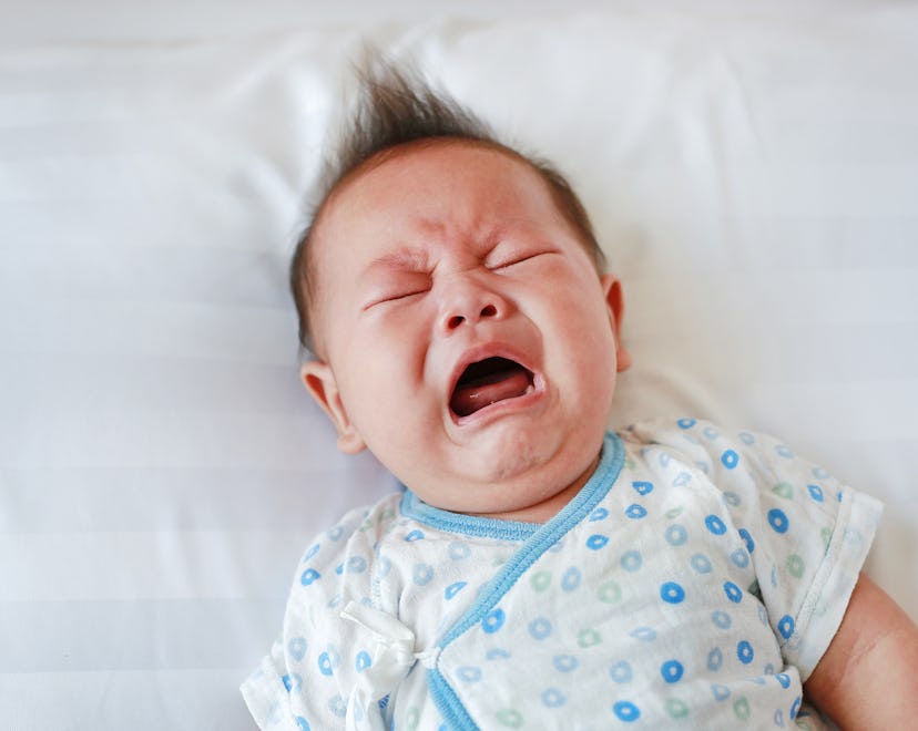 Portrait of infant baby boy crying and screaming lying on bed.