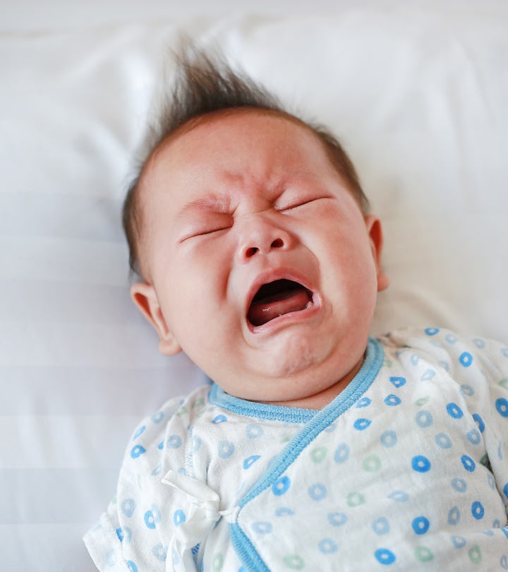 Portrait of infant baby boy crying and screaming lying on bed.