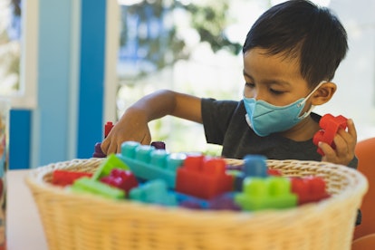 A young child wears an N95 face respirator mask while playing with blocks.