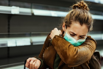 Sick woman buying in supermarket and coughing into elbow during COVID-19 pandemic. 