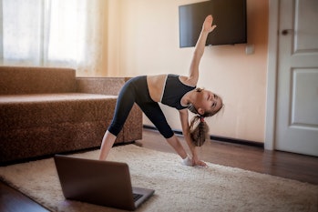 Pretty young girl in sportswear watching online video on laptop and doing fitness exercises at home....