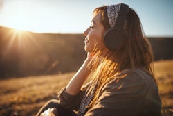A woman is outside during golden hour, lost in thought while listening to her headphone. Pisces zodi...