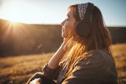 A woman is outside during golden hour, lost in thought while listening to her headphone. Pisces zodi...