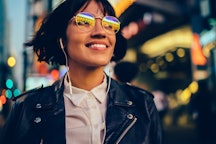 A smiling woman walks down a brightly lit city streets with glasses reflecting the light. An astrolo...