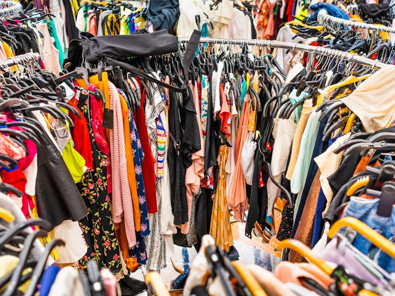 Crowded clearance section in a clothing store, with various colorful garments placed tightly on rack...